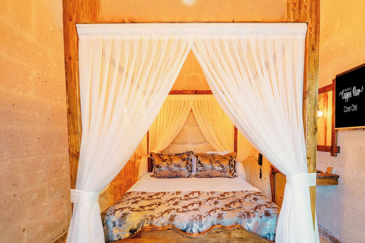 Um quarto com cama de dossel, parede de pedra e uma placa com a inscrição 'Cappo Niu Cave Otel'.