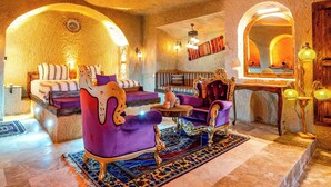 Ein Zimmer mit einem Bett, einem violetten Sessel, einem Holzhocker und einem kleinen Tisch mit Teppich.