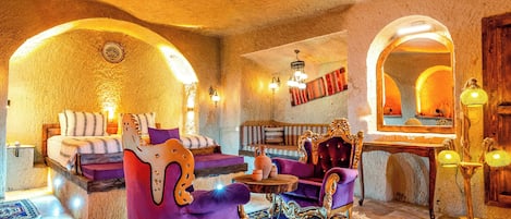 Una habitación con una cama, un sillón morado, una silla de madera y una pequeña mesa con un tapete.