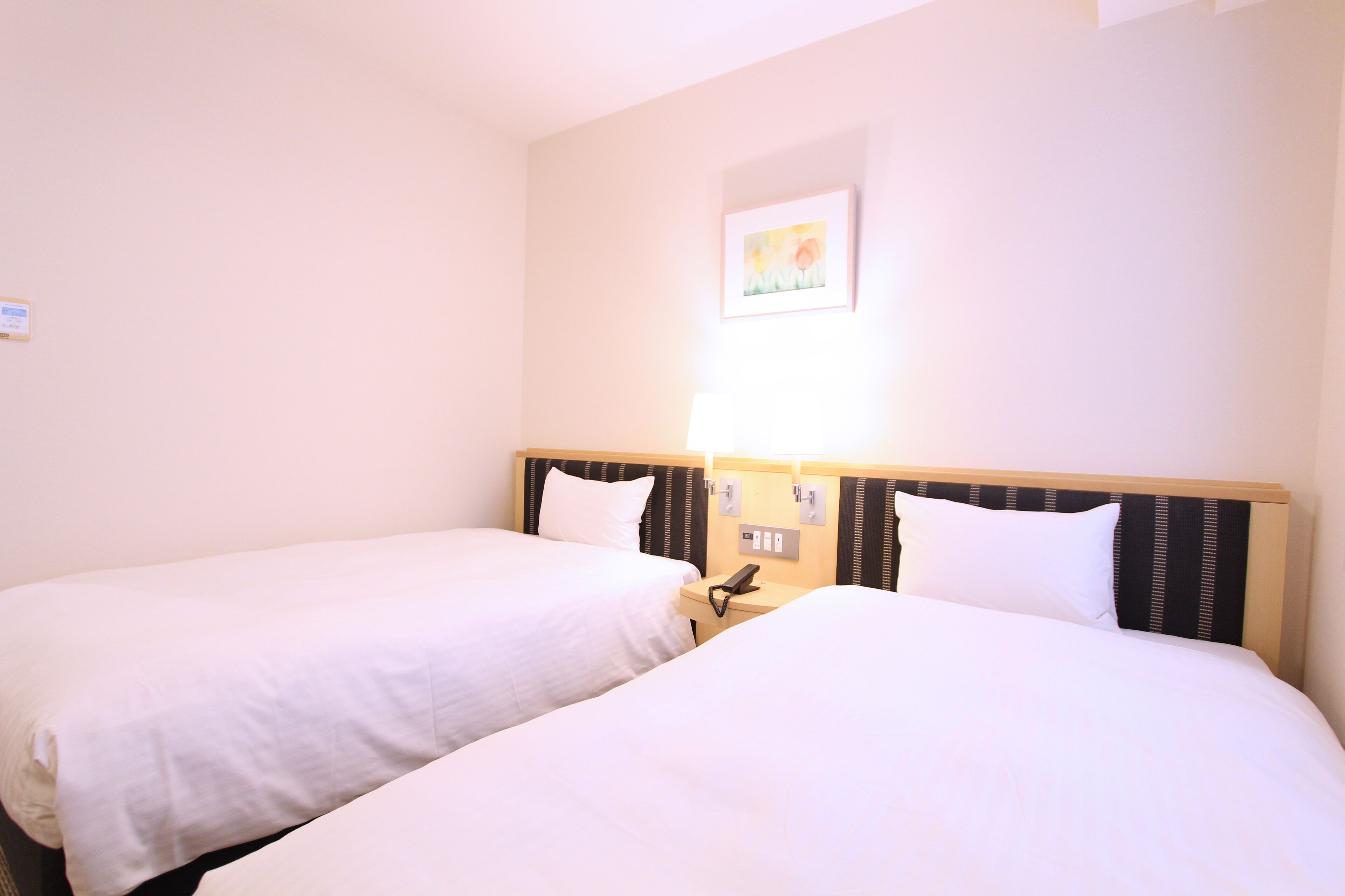 A hotel room with two single beds, a bedside table with a phone, and a wall-mounted light.