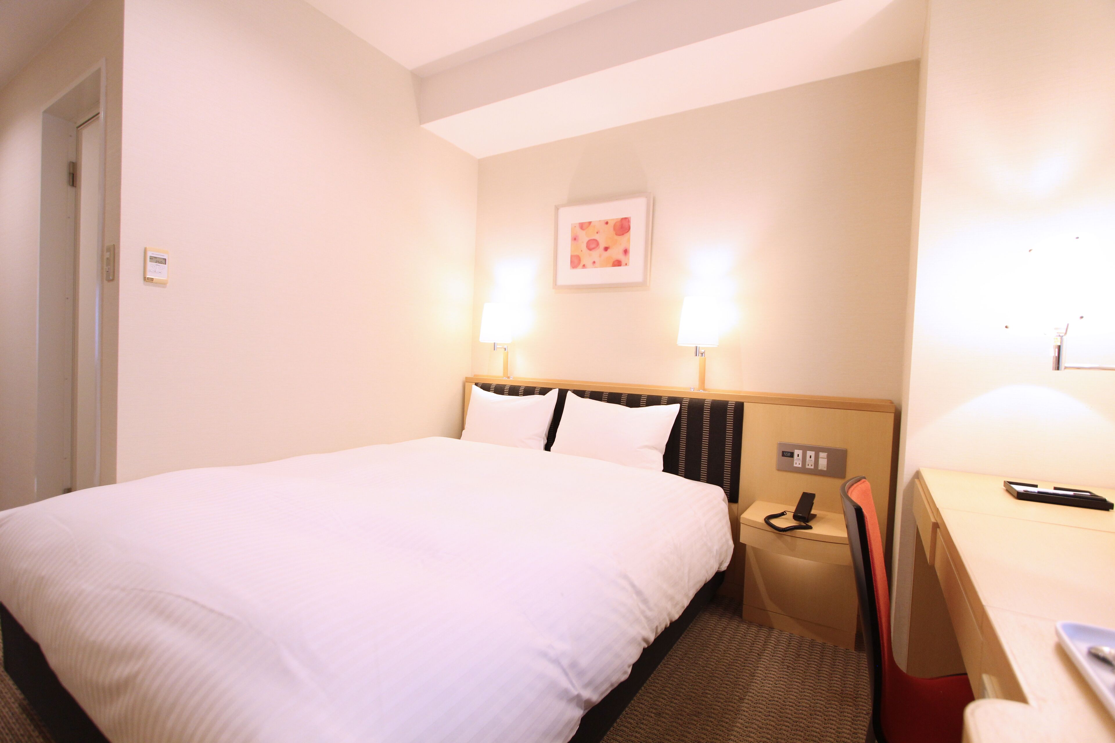 A hotel room with a large bed, bedside lamps, a desk, and a chair.