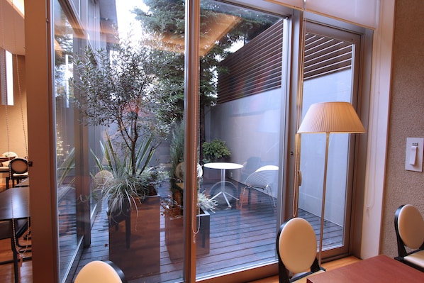 A modern room with a glass door leading to an outdoor patio. Inside, there is a wooden table with two chairs, a floor lamp, and a small potted plant. - KOKO HOTEL Sendai Station West (Sendai)