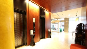 Eine moderne Hotelhalle mit einem Holzbuchtschalter, einer roten Sitzgruppe und einem sichtbaren Aufzug.