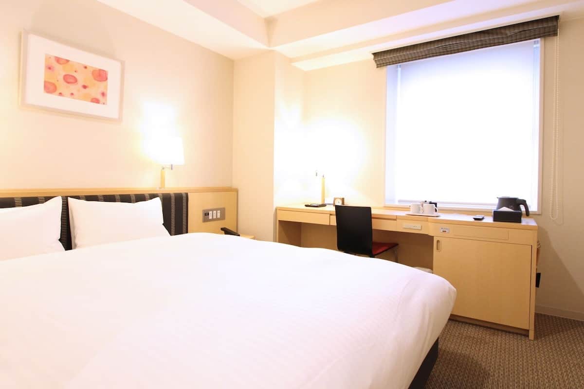 A hotel room with a bed, desk, chair, and a window with a view.