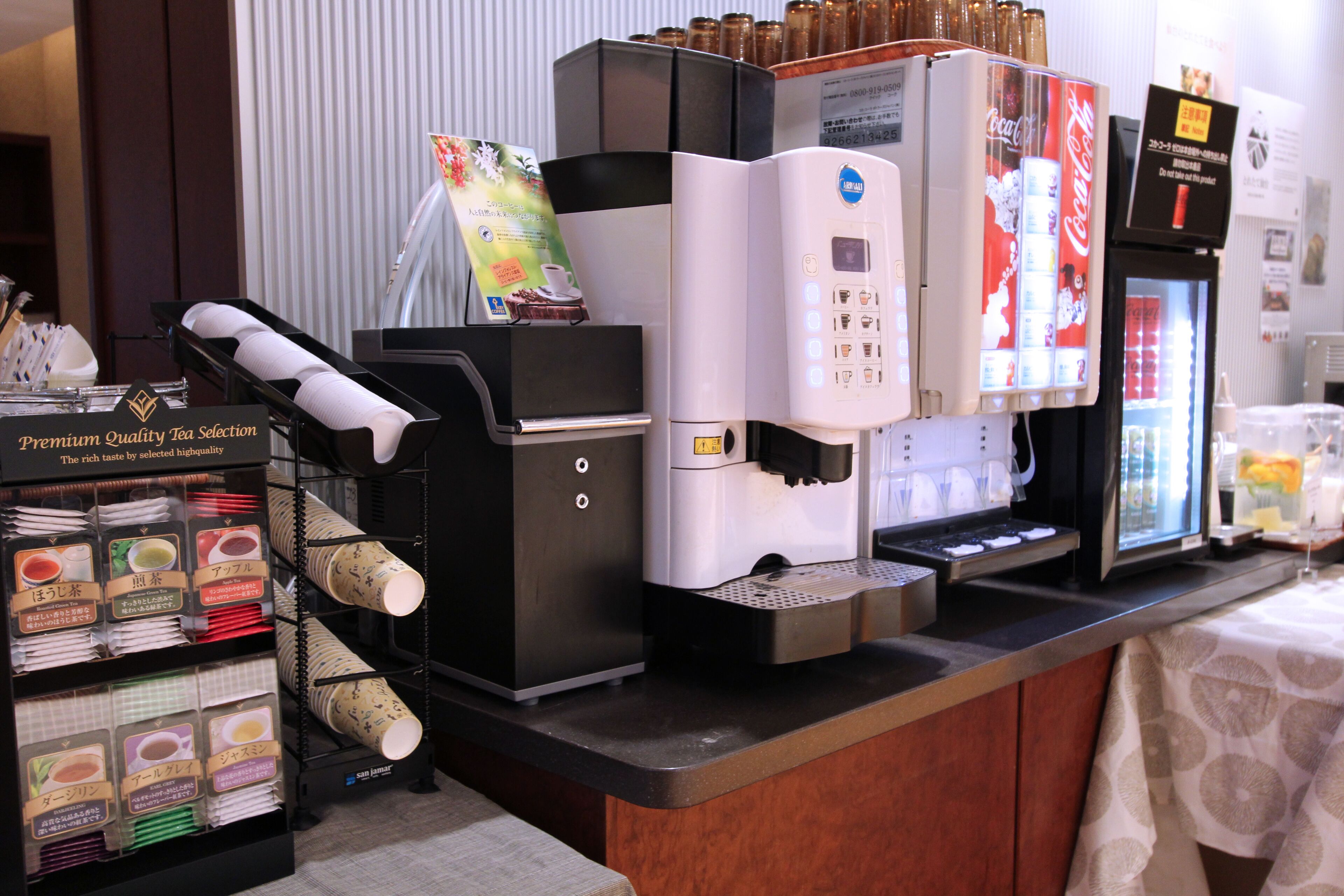 A coffee station with multiple coffee machines, a tea selection display, and a Coca-Cola refrigerator.