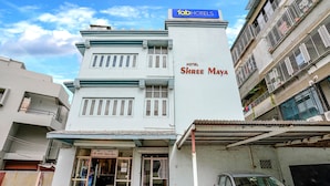 Hotel Shree Maya con letrero, un coche estacionado adelante y un edificio vecino con balcones.