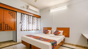 Un dormitorio con cama, cabecera de madera, ventana con cortinas estampadas y armario empotrado.
