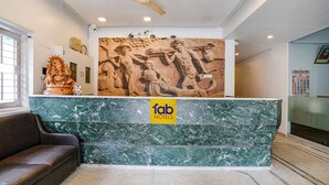 Zona de recepción de un hotel con mostrador de mármol, ventilador de techo y un mural en la pared.