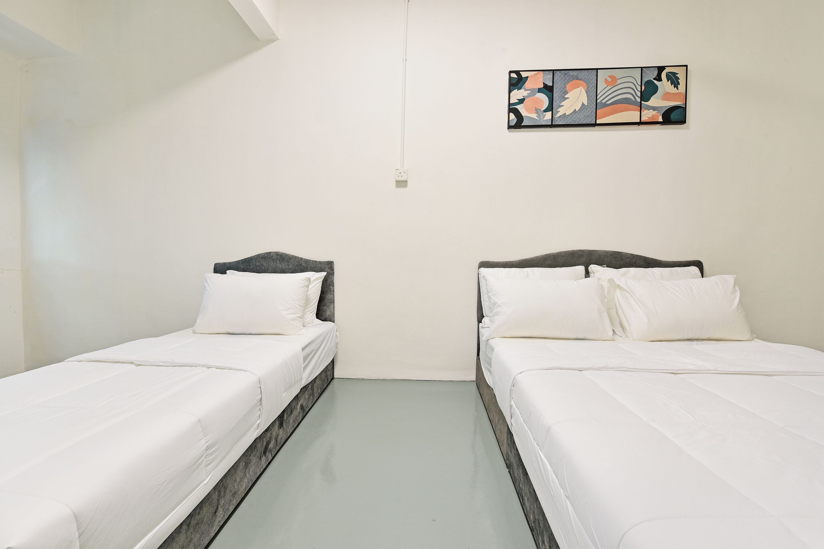 A room with two single beds, white bedding, a light-colored floor, and a wall-mounted abstract art piece.