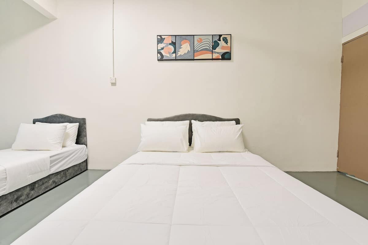 A hotel room with a large bed, two single beds, a painting on the wall, and a plain white wall.