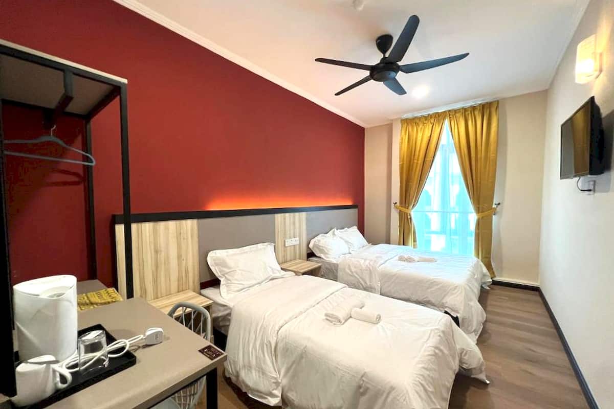 A hotel room with two beds, a desk with a coffee maker, a TV, and a ceiling fan.