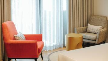 Ein Hotelzimmer mit einem roten Sessel, einem beigen Sessel, einem runden Beistelltisch und einem Bett.