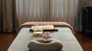 A massage table with a cushion, a glass teapot, a glass, and a folded towel.
