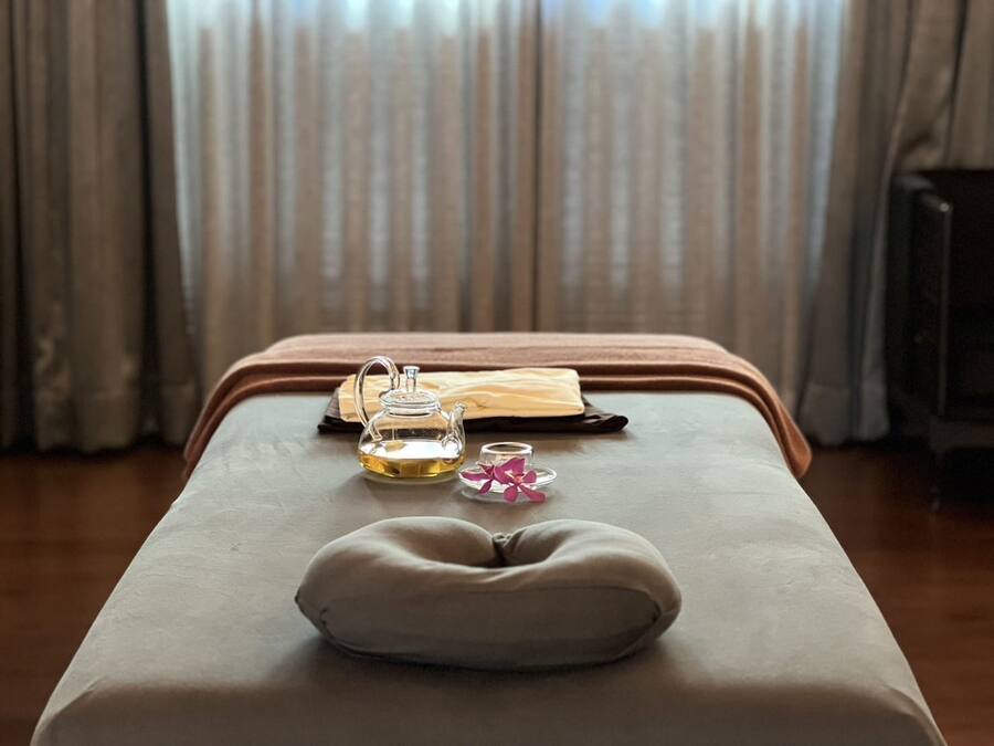 A massage table with a cushion, a glass teapot, a glass, and a folded towel.