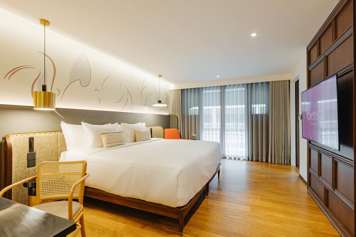Ein modernes Hotelzimmer mit einem großen Bett, einem Fernseher, Holzboden und einer Wandleuchte.