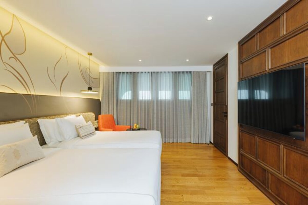 Een hotelkamer met een groot bed, een televisie, houten lambrisering en een raam met gordijnen.