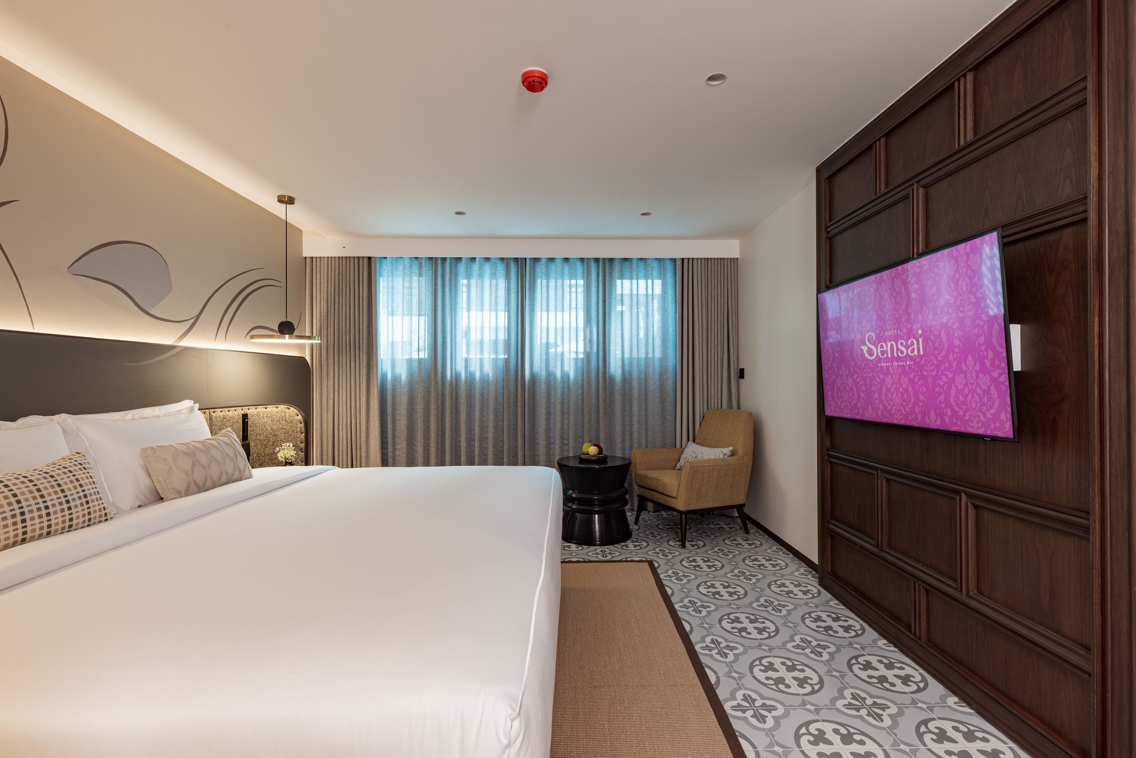 A hotel room with a large bed, a TV, a chair, and a small table with fruit.