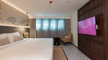 A hotel room with a large bed, a TV, a chair, and a small table with fruit.