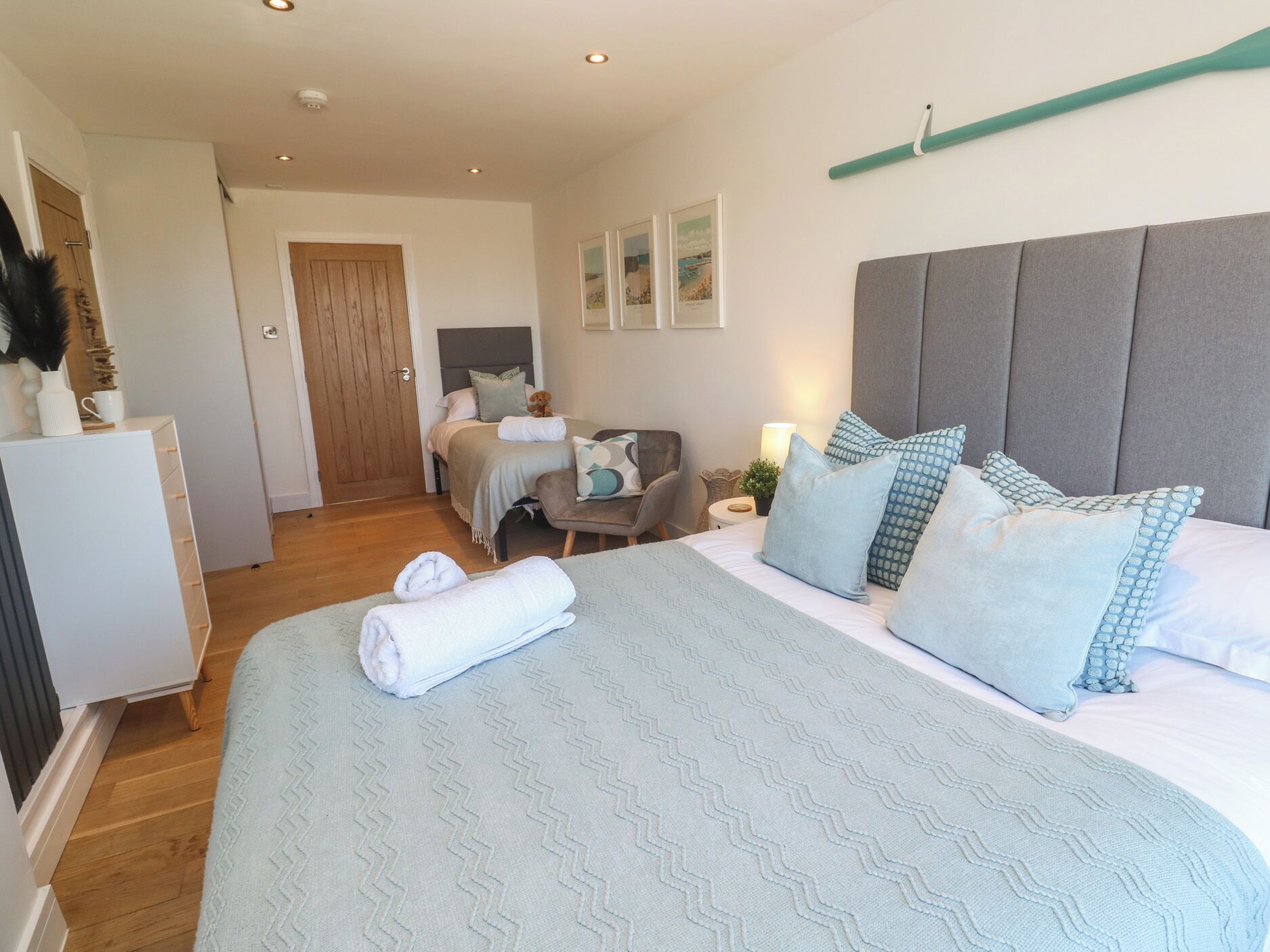 A bedroom with a large bed, a bedside table with a lamp, a chair, a desk, and a wardrobe.