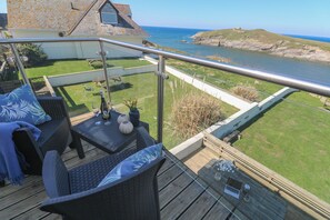 A deck with wicker furniture, a table with a bottle and glasses, and a view of the sea and cliffs. - Island View (Newquay)