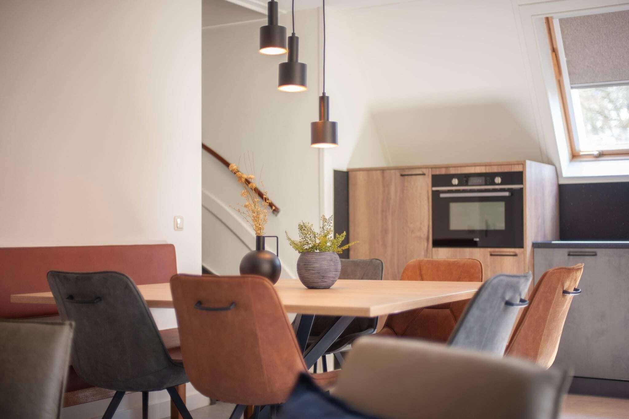 A modern dining area with a wooden table, black and brown chairs, and pendant lighting.