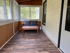 Een overdekt terras met een bankje en een tafel, houten vloeren en uitzicht op de omgeving.
