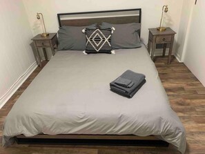 A bed with a white mattress, two pillows, a folded blanket, and two bedside tables with lamps. - Catskills Brookside Cottage (Margaretville)