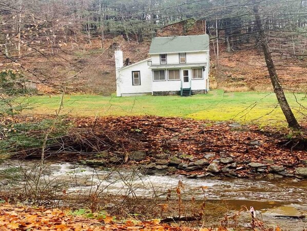 A house with a stone wall in front, a grassy area, and a stream.