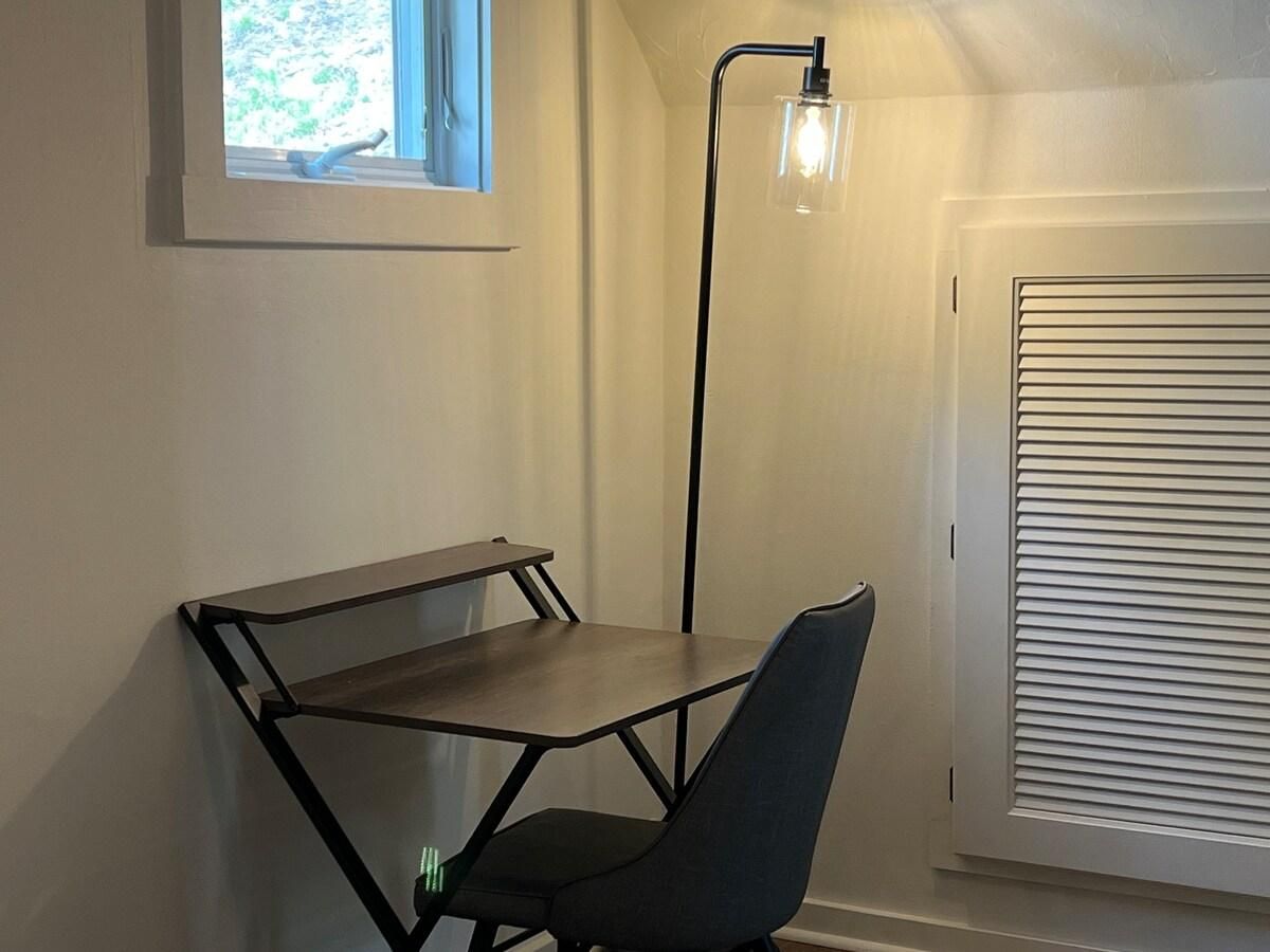 A compact workspace with a desk and chair, a floor lamp, and a window with blinds.
