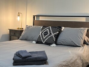 A neatly made bed with pillows, a bedside lamp, and a folded blanket on a wooden headboard. - Catskills Brookside Cottage (Margaretville)