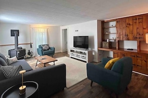 A modern living room with a sofa, armchair, TV, and a fireplace. - Catskills Brookside Cottage (Margaretville)