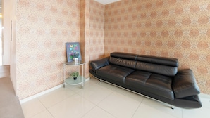 A living room with a black leather sofa, patterned wallpaper, and a small side table with a potted plant. - Collection O 88 Hotel (Malacca City)