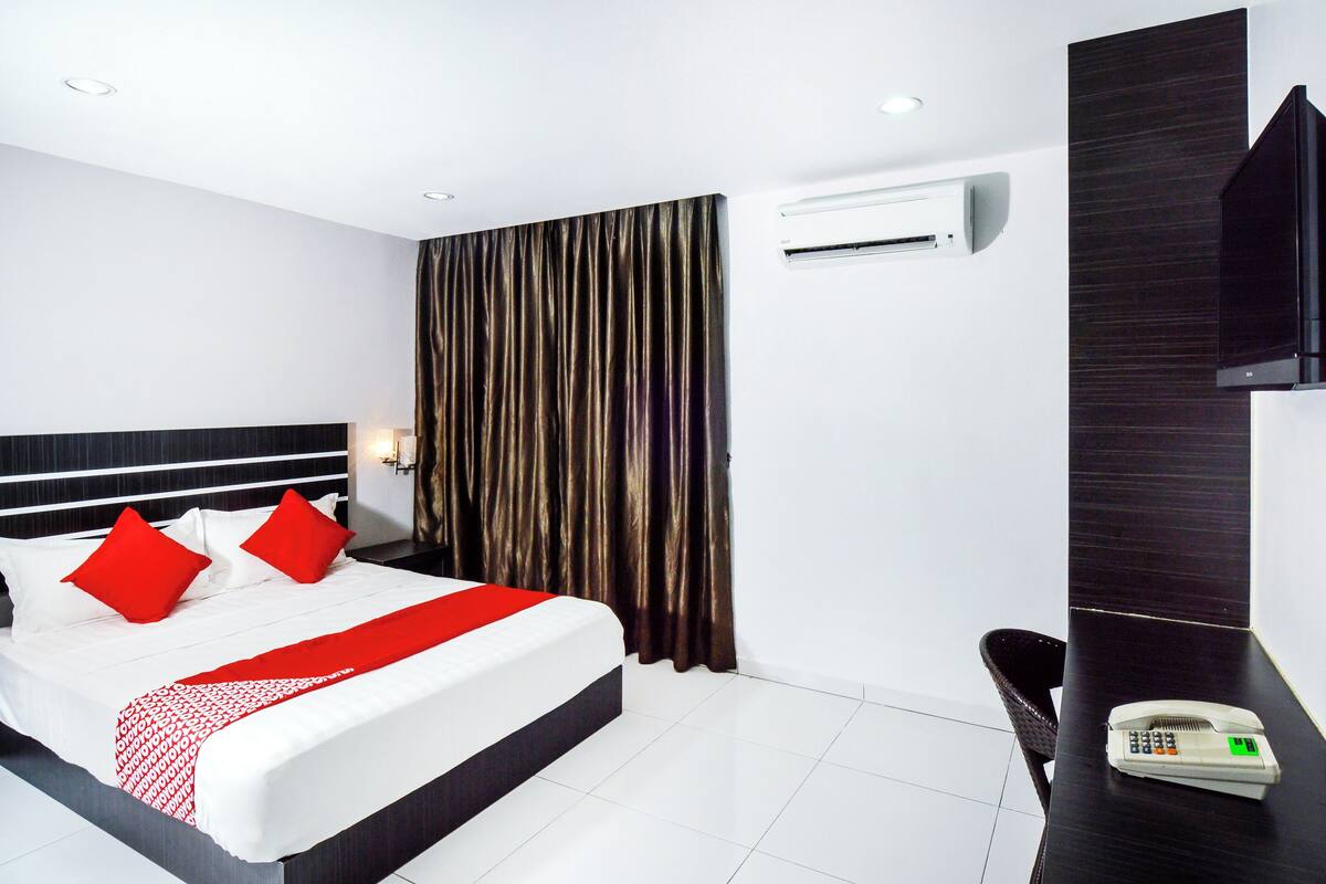 Een hotelkamer met een netjes opgemaakt bed, een bureau met telefoon en een airconditioning aan de muur.