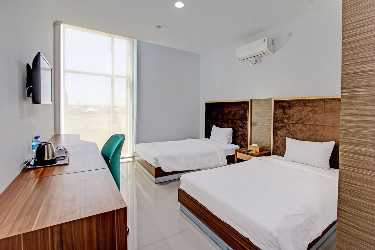 A hotel room with two beds, a desk, a chair, a TV, and a window.
