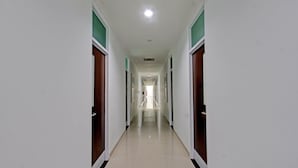 A long, narrow hallway with doors on both sides, leading to a bright room at the end. - Capital O 92604 Hotel Uin Syariah Near Kampus UIN Mataram (Mataram)
