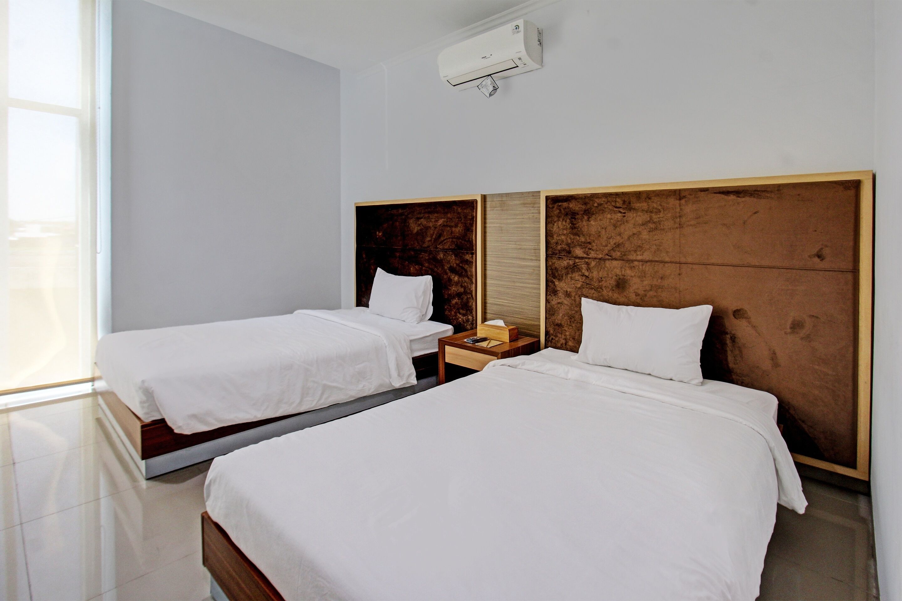 Een hotelkamer met twee bedden, een nachtkastje en een luchtverkoeler aan de muur.