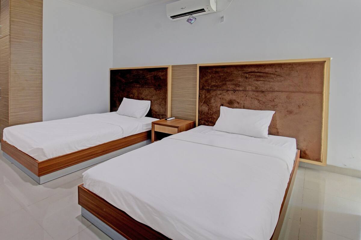 A hotel room with two beds, wooden headboards, white bedding, and a small bedside table.