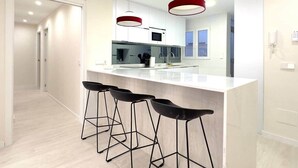 A modern kitchen with a white countertop, black bar stools, and red pendant lights.