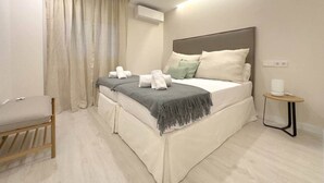 A modern hotel room with a large bed, a bedside table, a chair, and an air conditioning unit.