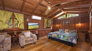 Un dormitorio estilo cabaña acogedor, con paredes de madera, una cama grande con colcha floral, un televisor y una ventana con cortinas.