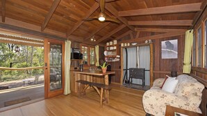 Interior acogedor de una cabaña con techo de madera, comedor con banco, sofá y zona de cocina con microondas y cafetera.