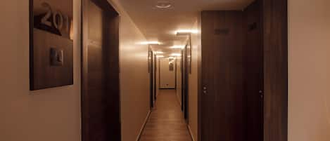 Un long couloir étroit, avec des portes en bois et un luminaire au plafond.
