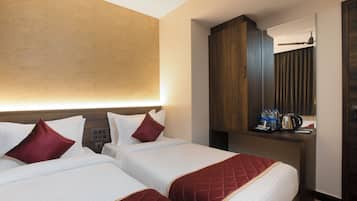 A hotel room with two beds, a wooden wardrobe, a desk with a mirror, and a nightstand with a kettle and bottles.