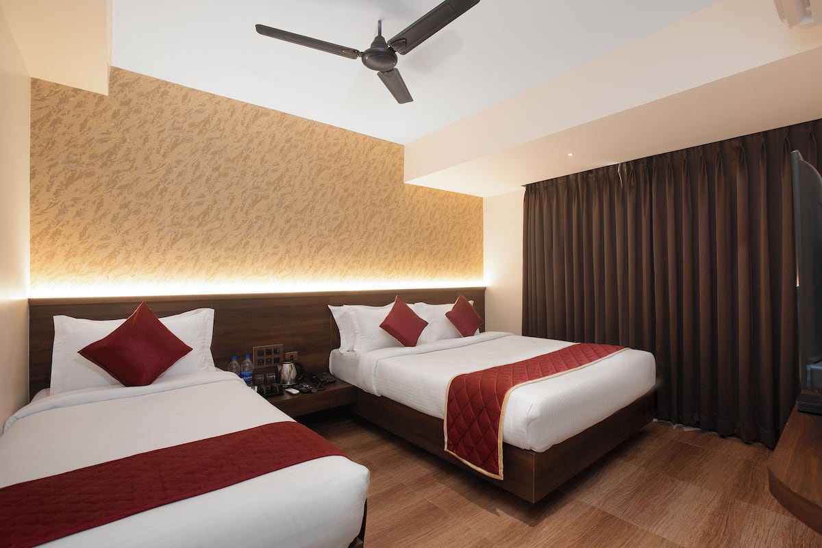A hotel room with two beds, a ceiling fan, a headboard with a textured wall, and a large window with curtains.