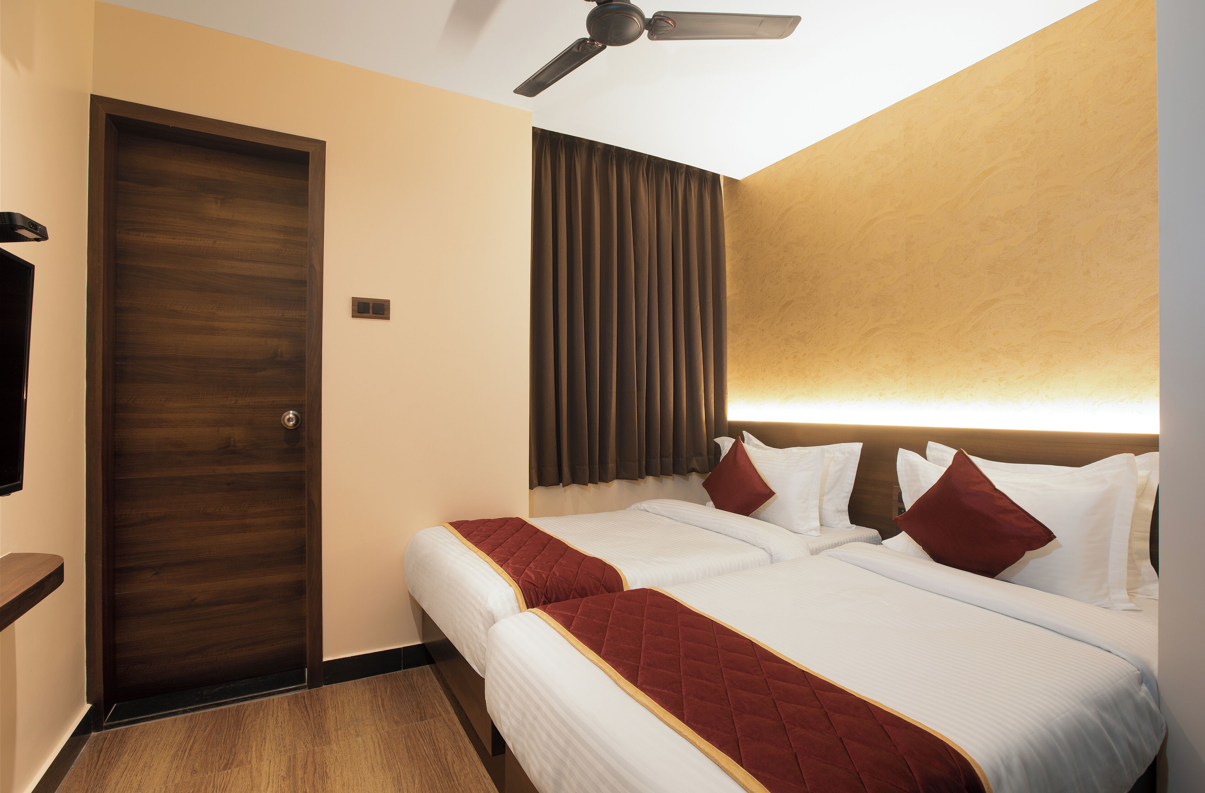 A hotel room with two beds, a ceiling fan, a wooden door, and a curtain.