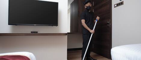 Egy szállodai szoba, amelyben van egy ágy, a falra szerelt televízió, és egy személy éppen felmos.