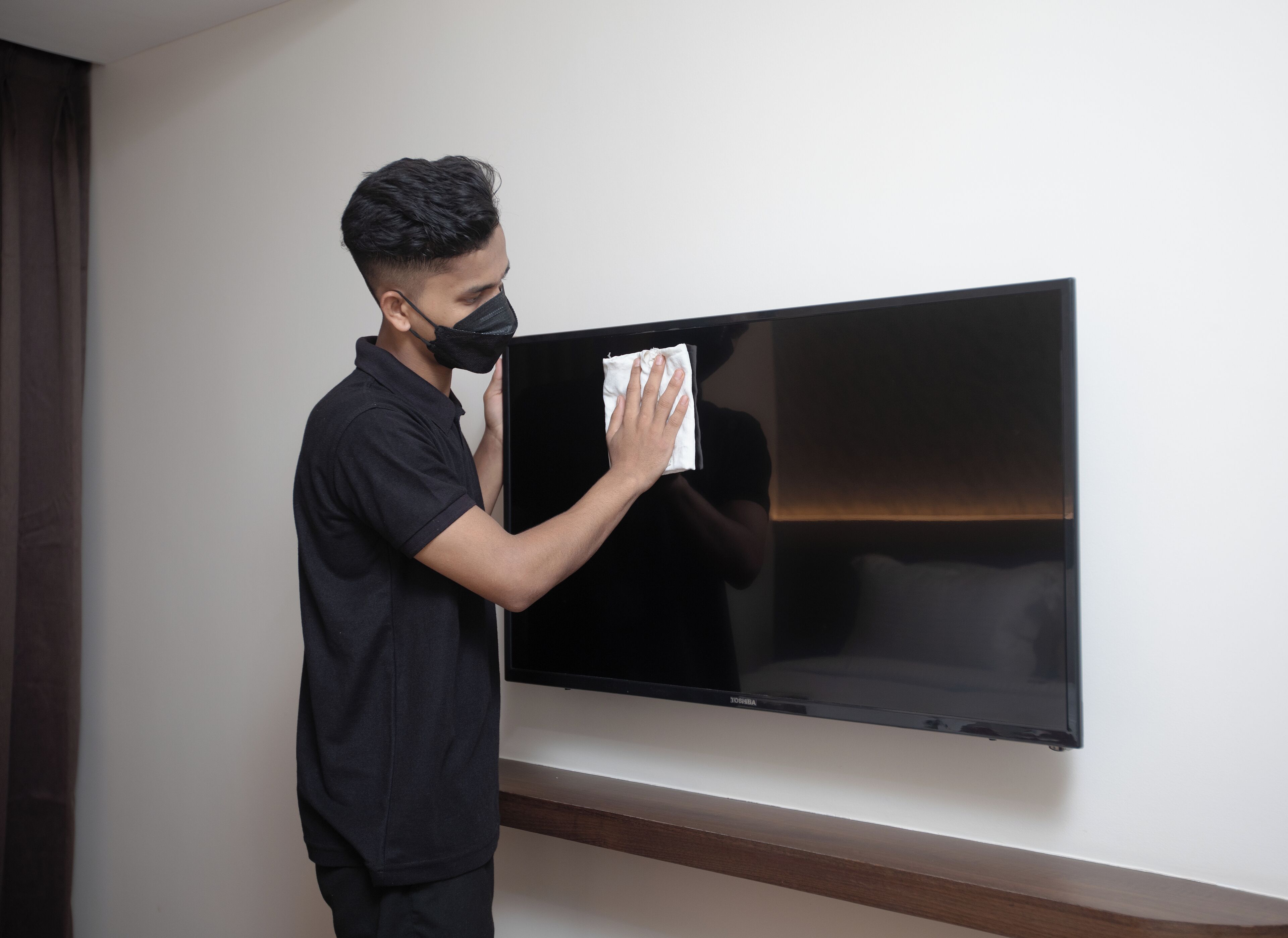 Una persona limpiando un televisor de pantalla plana montado en la pared.