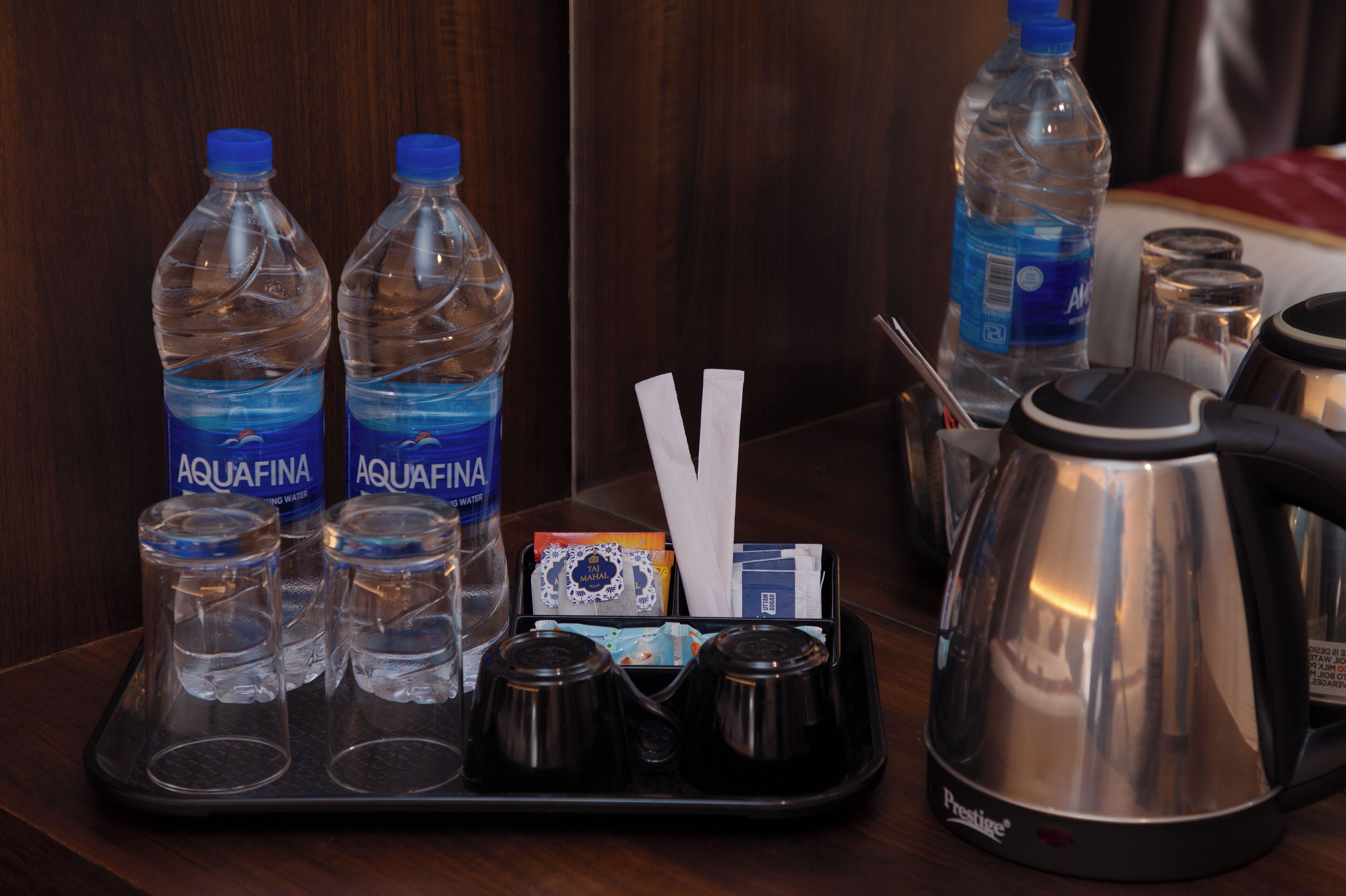 A tray with water bottles, glasses, a kettle, and some packets on a wooden surface.