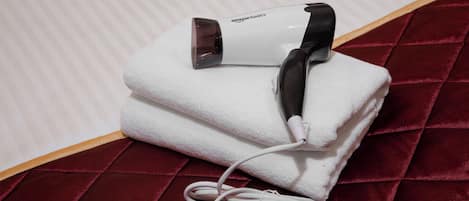Un sèche-cheveux portable blanc de la marque Amazon Basics, posé sur une serviette blanche, lui-même placé sur une surface en velours rouge.