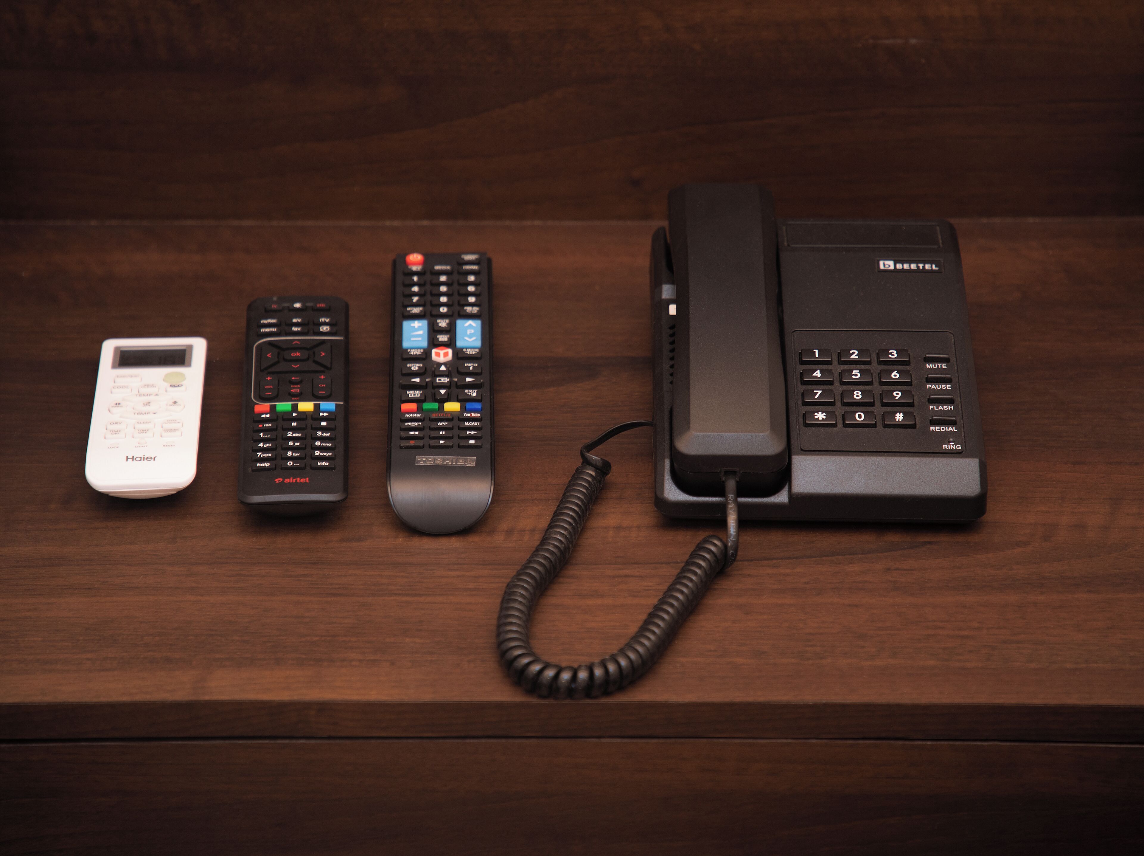 Una superficie de madera con cuatro controles remotos y un teléfono.